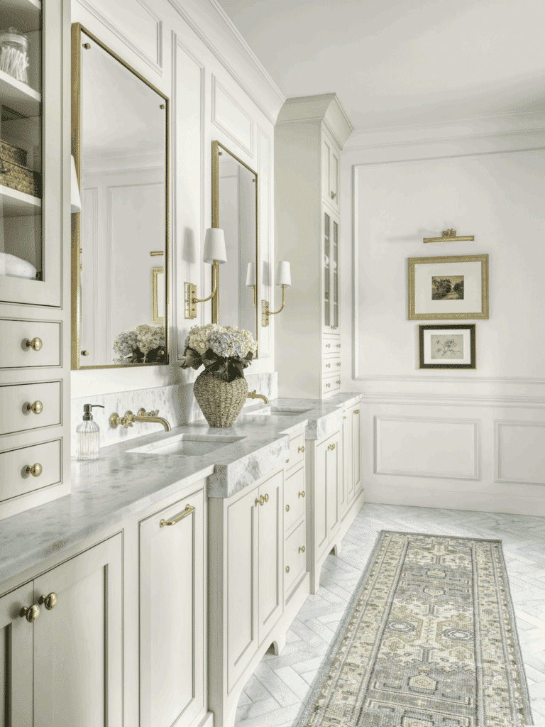 Bright master bathroom renovation with dual sinks, marble countertops, brass faucets, and gold-framed mirrors.