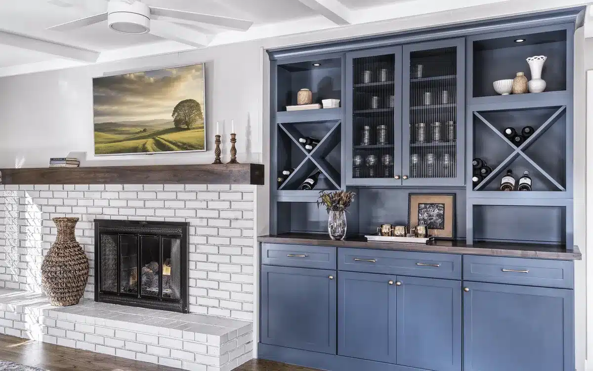 Blue built-in cabinetry unit next to a white brick fireplace with a dark wood mantel and mounted television.